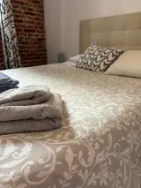 Primer plano de la cama doble con toallas dobladas y cojines junto al cabecero y la pared de ladrillo